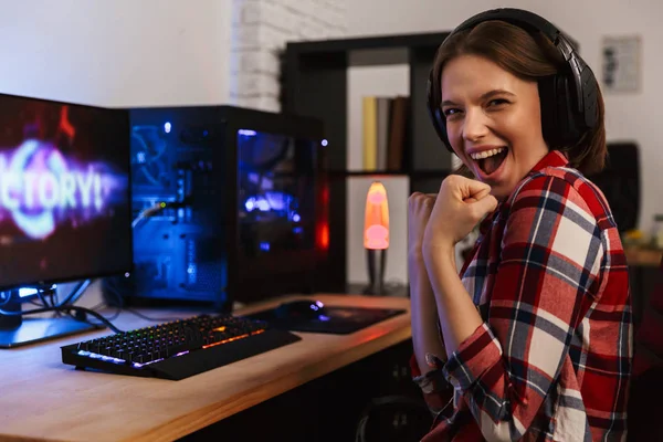 A smiling player at a desk in headphones beside a warm glowing lamp and a small bookshelf